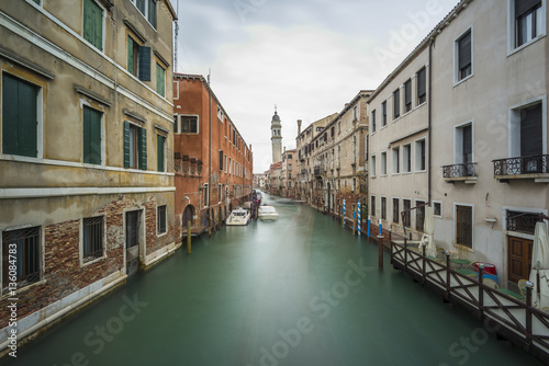 Long time exposure of canal in Venice (Venezia) with old buildings, boats and the leaning belfry tower of San Giorgio dei Greci, Italy, Europe © AR Pictures
