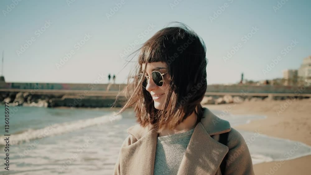 Portrait of sexy and beautiful brunette girl in sunglasses looks at camera, smiles and plays with her dark hairs at sunny windy winter day on empty beach next to sea Escaping from town to quiet place Portrait of sexy and beautiful brunette girl in sunglasses looks at camera, smiles and plays with her dark hairs at sunny windy winter day on empty beach next to sea Escaping from town to quiet place