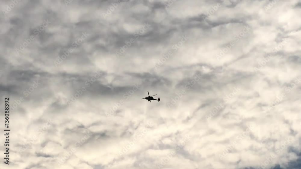 A Military Apache Attack Helicopter flies overhead silhouetted against a cloudy sky A Military Apache Attack Helicopter flies overhead silhouetted against a cloudy sky