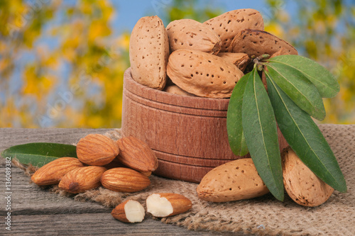 almonds with leaves in a bowl on the old wooden board  blurred garden background photo