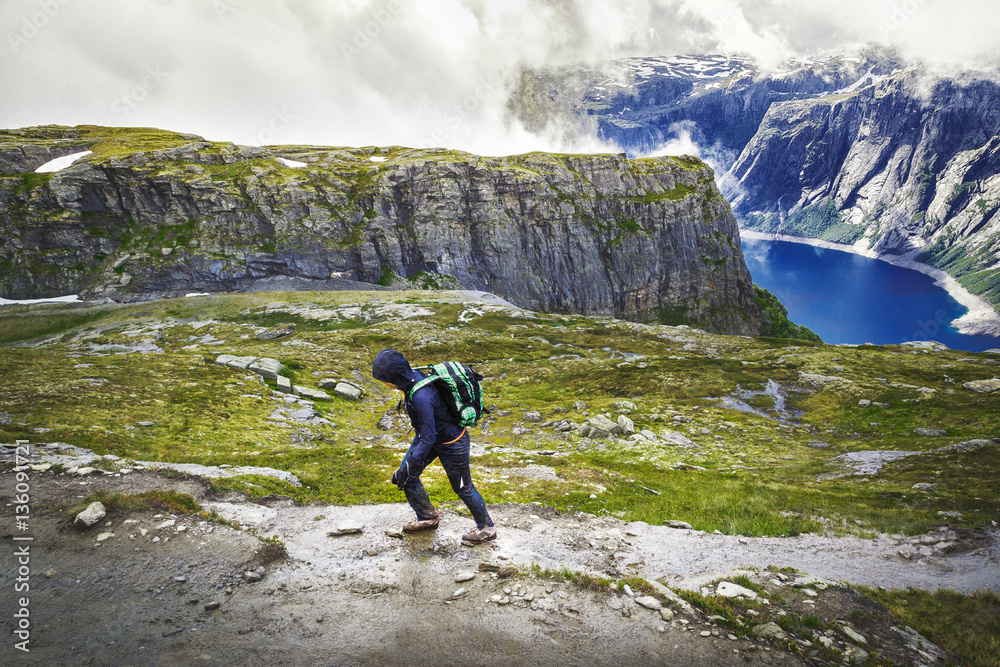 Hiker with backpack walking up to summit in Norway mountains by trail to Trolltunga nature attraction. Fitness and healthy lifestyle outdoors at wild pristine nature background.