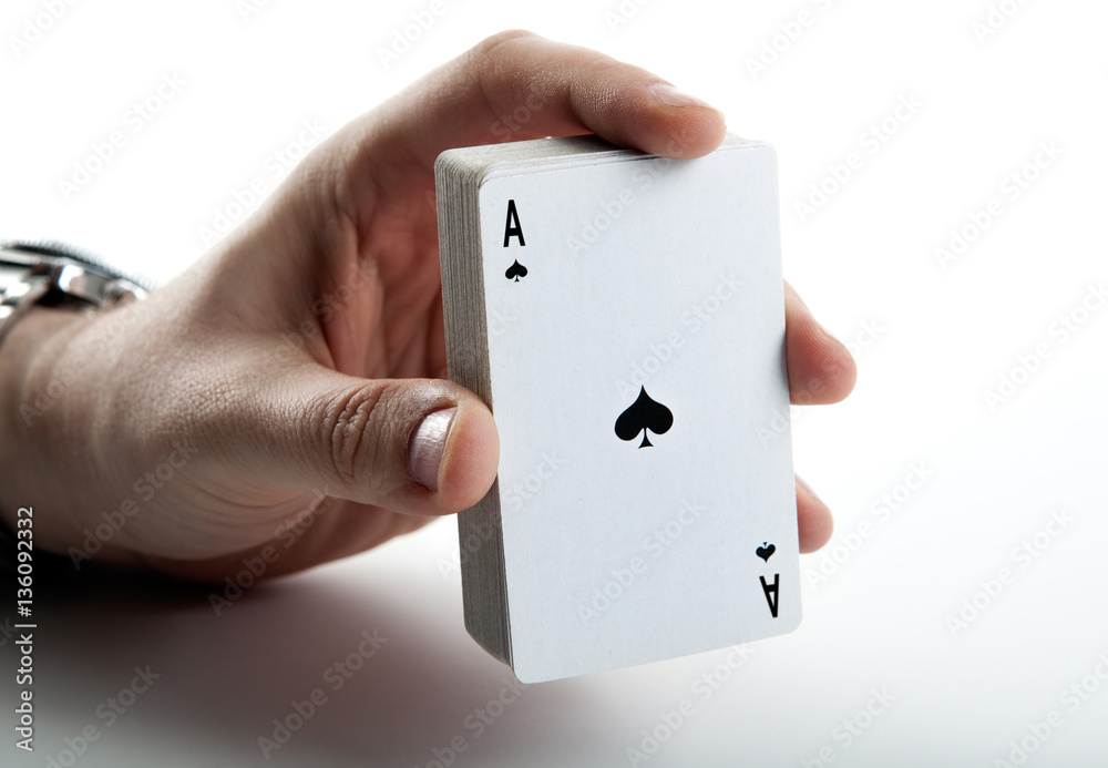 Human hand holding the ace of spades and a deck of cards