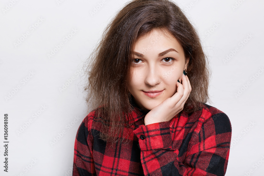 Beautiful young brunette woman in a red checked shirt holding her hand on chin looking confident into the camera isolated over white background. A confident expression of pretty girl Beautiful young brunette woman in a red checked shirt holding her hand on chin looking confident into the camera isolated over white background. A confident expression of pretty girl