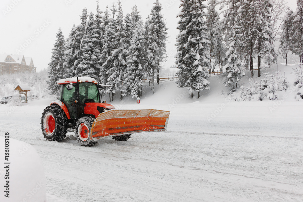 Red snowblower grader clears snow covered ski resort road in mountains or city street. Winter snowflake snowfall cold fog, mist weather. Horizontal, copy space.