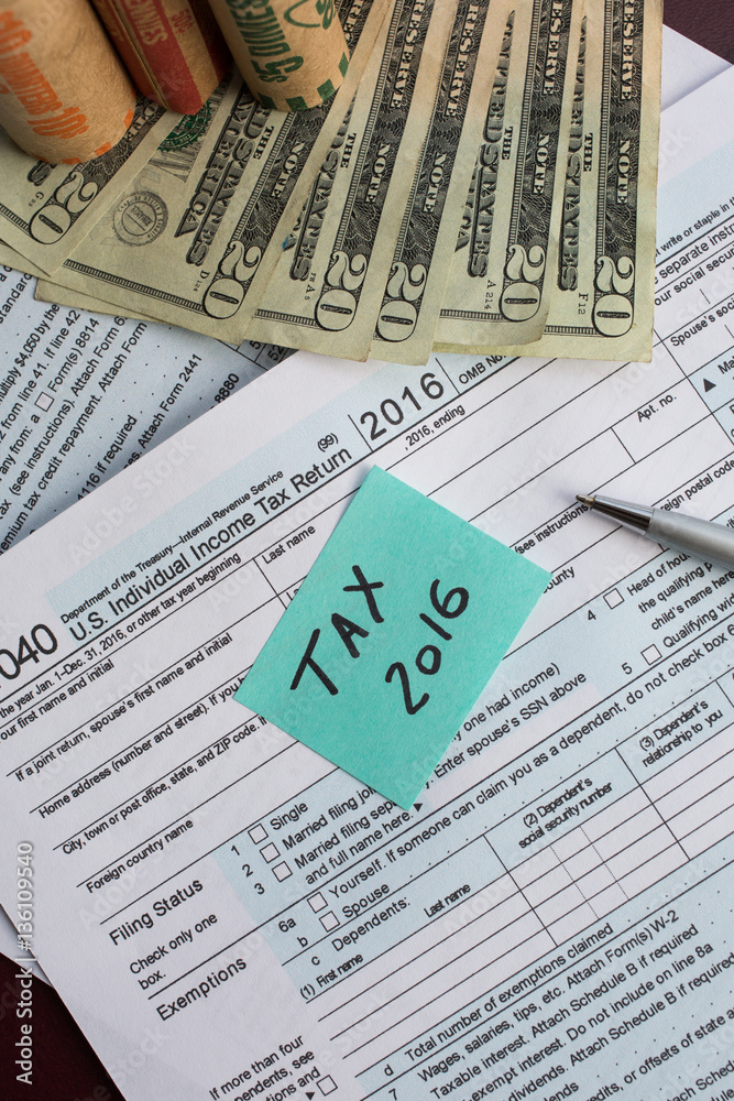 Tax time 2016 written on a written on a bright sticker and tax form 1040 with pen and twenty dollars banknotes US 1040 tax form with coin wrappers Tax time 2016 written on a written on a bright sticker and tax form 1040 with pen and twenty dollars banknotes US 1040 tax form with coin wrappers