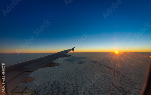aircraft window view of wing with setting sun and deep blue sky and clouds below  (A320)