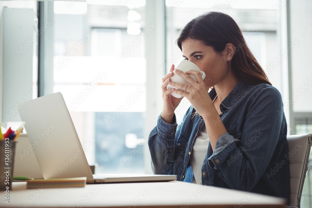 Business executive having cup of coffee while using laptop Business executive having cup of coffee while using laptop