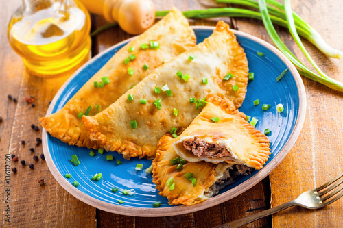 Traditional Romania, Ukrainian, Russian and Tatar food cheburek with meat and spring onion. National east meal. Meat pastry on a blue plate. Top view.