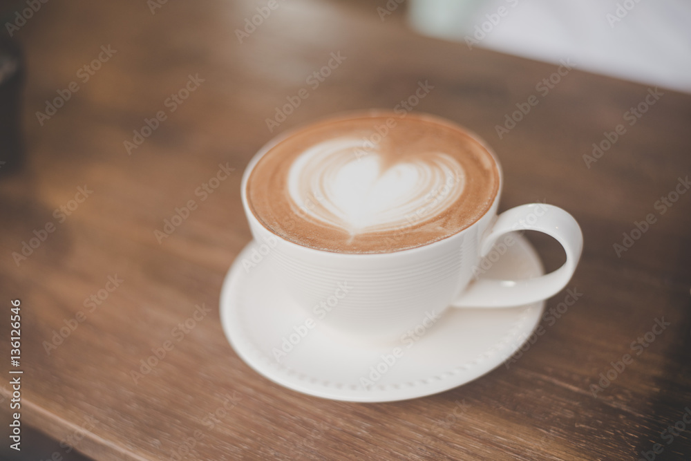 Hot art latte coffee with heart shape in a cup on wooden table.