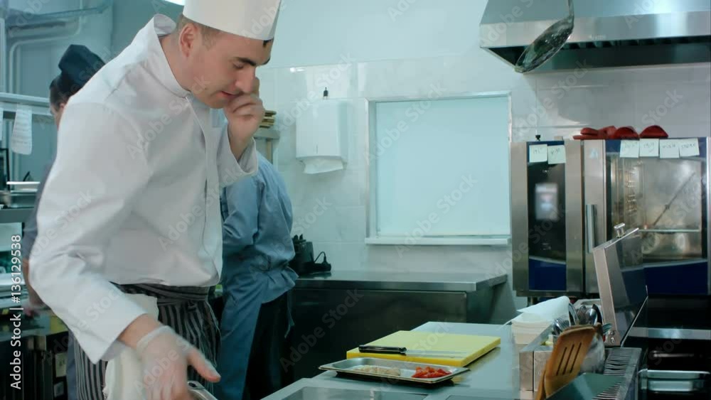 Chef talking on the phone and tossing ingredients on a frying pan in the restaurant kitchen Chef talking on the phone and tossing ingredients on a frying pan in the restaurant kitchen