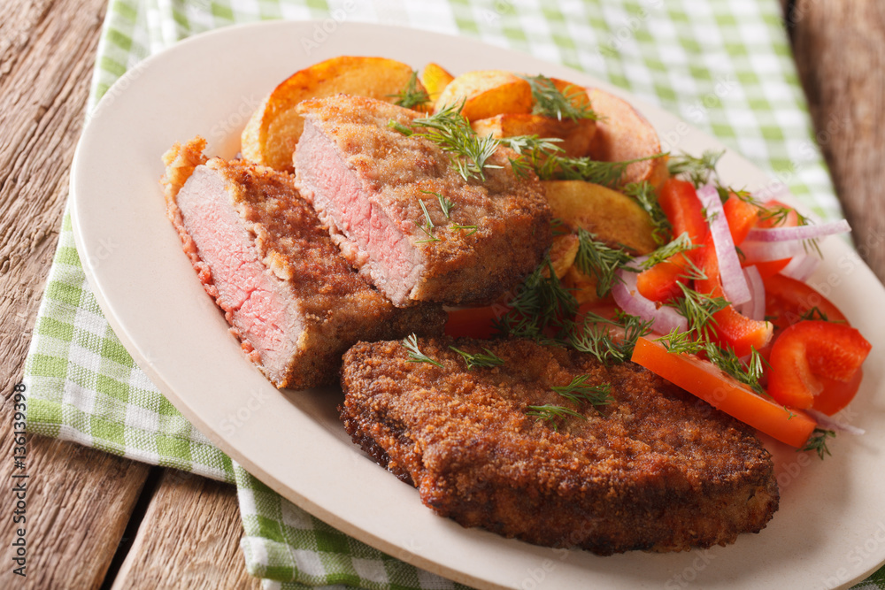 Breaded round steak and a side dish of vegetables close-up. horizontal