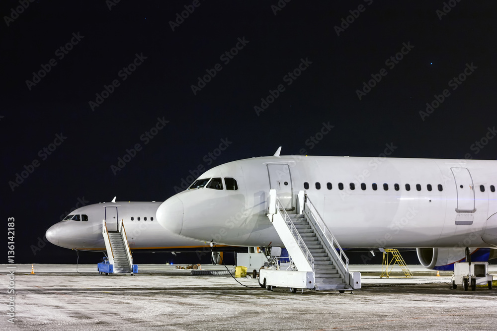 The front part of the two aircraft with passenger boarding stairs at night winter airport apron The front part of the two aircraft with passenger boarding stairs at night winter airport apron