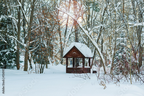Wooden gazebo in the snow in winter forest background © golubka57