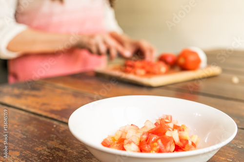 Mujer cortando tomate para una receta en casa. 