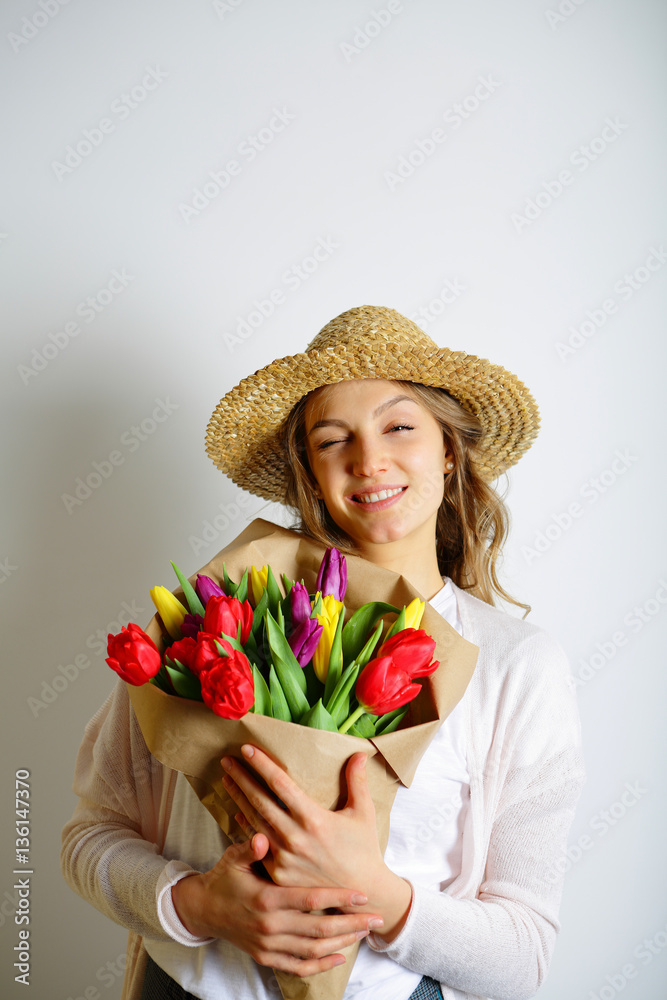 Girl in a straw hat winking at the camera, holding a bouquet of