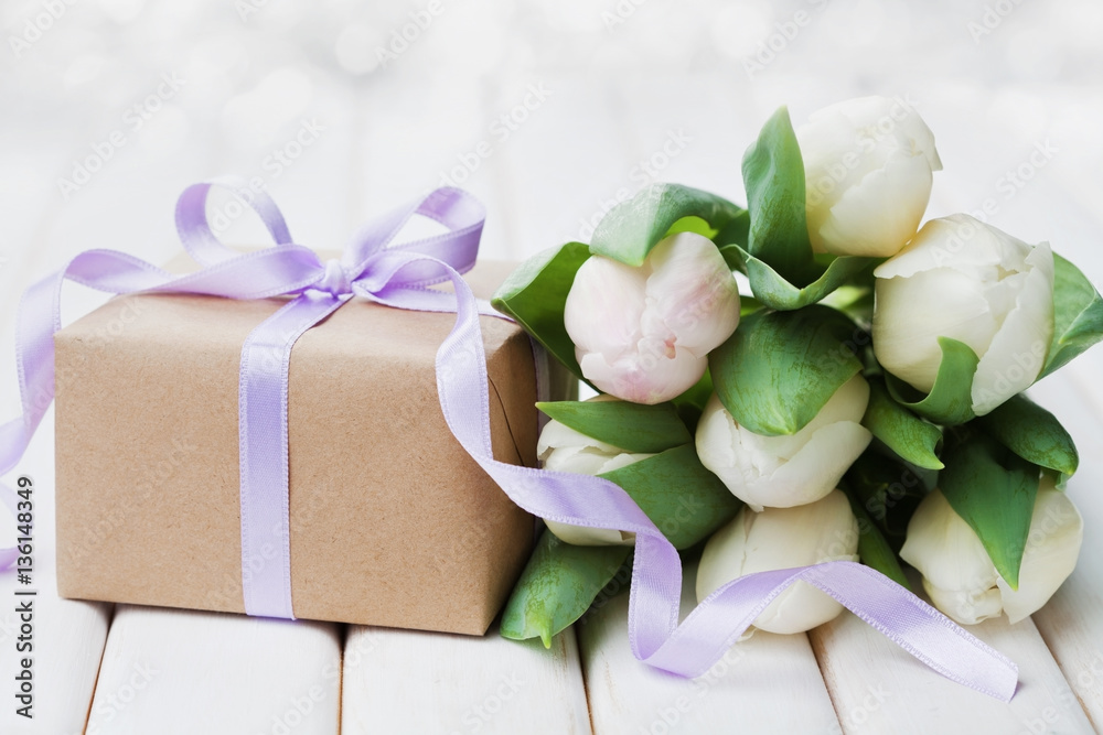 Spring tulip flowers and gift box with bow ribbon on white table. Greeting card for Birthday, Womens or Mothers Day. Spring tulip flowers and gift box with bow ribbon on white table. Greeting card for Birthday, Womens or Mothers Day.