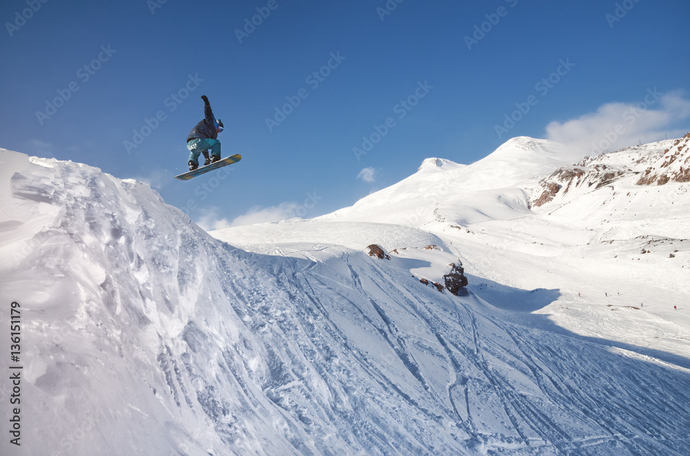 Stylish snowboarder with helmet and mask jumps from high snow slope