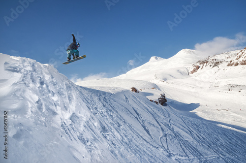 Stylish snowboarder with helmet and mask jumps from high snow slope