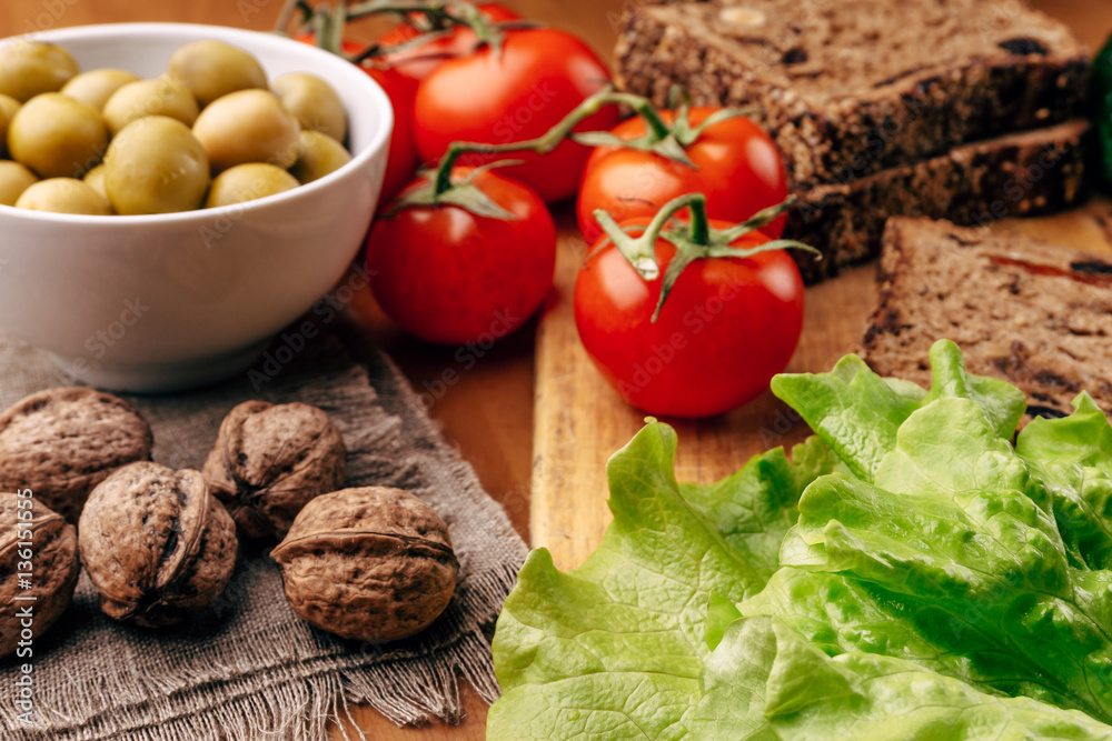 Homemade bread on wooden board, fresh tomatoes, olives in bowl, walnuts Homemade bread on wooden board, fresh tomatoes, olives in bowl, walnuts