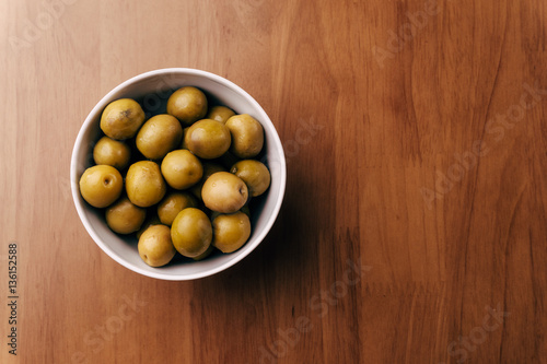 Fresh green olives in white bowl on wooden table background. Top view with copy 