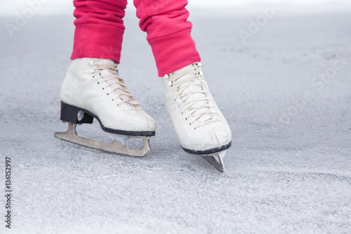 Woman skating and training with white skates on the ice area in winter day. Weekends activities outdoor in cold weather.