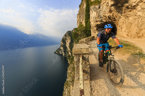 Mountain biking at sunrise man over Lake Garda on path Sentiero