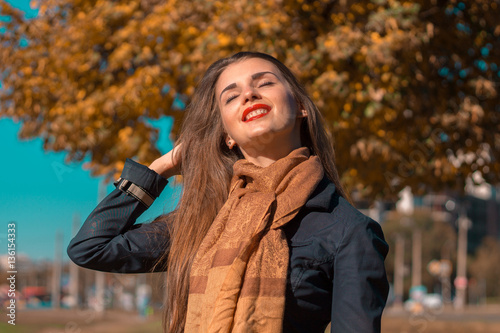 young girl in a warm scarf raised hand to her hair and smiles