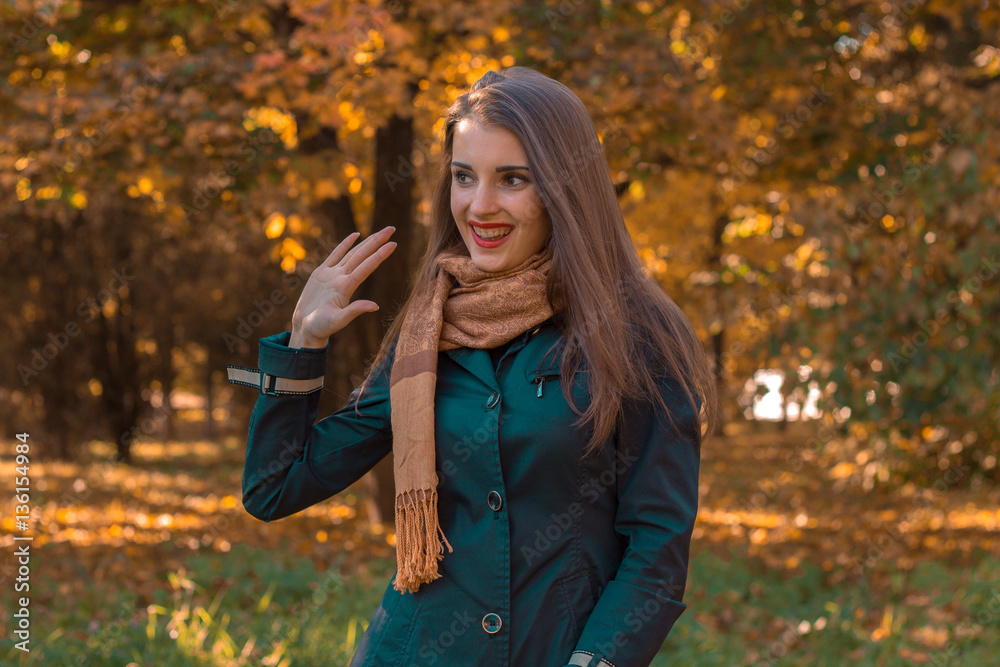 smiling young woman with a scarf on the shoulders of stands in the Park and smiles smiling young woman with a scarf on the shoulders of stands in the Park and smiles