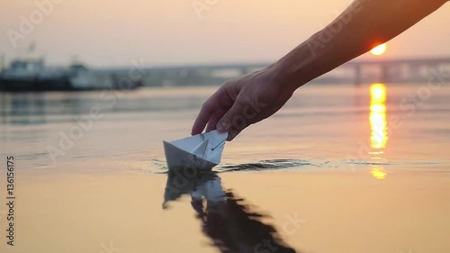 Man's hand putting paper boat on the water and pushing it away during beautiful sunset with reflection sun in the sea in slowmotion. 1920x1080