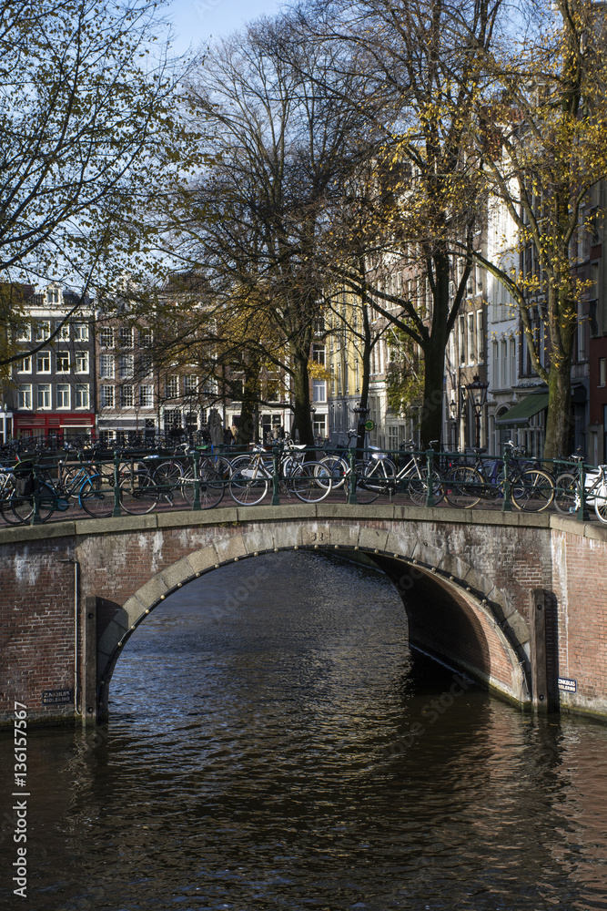 Brown bridge with bikes over the canal in autumn in the day in Amsterdam