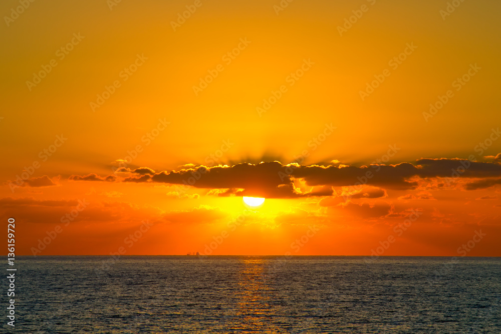 Orange sunset with rays shines through the clouds at Paphos coas