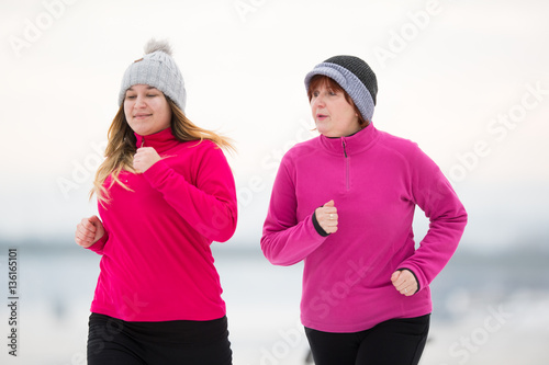 Mother and daughter wearing sportswear and running on snow durin photo