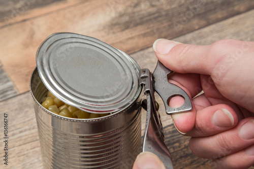 Old opener open to metallic can on the table in the kitchen. Canned corn in the can. Healthy eating and lifestyle. photo