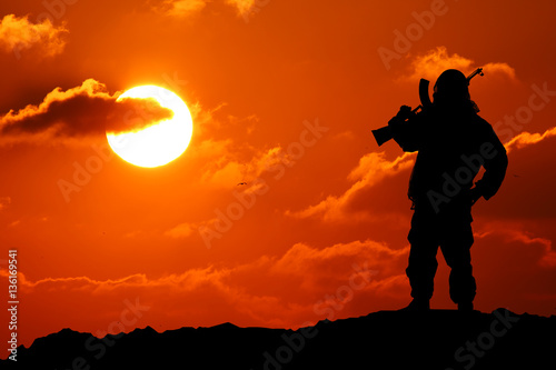 Silhouette shot of a soldier holding a gun with a picturesque mountain backdrop at sunset