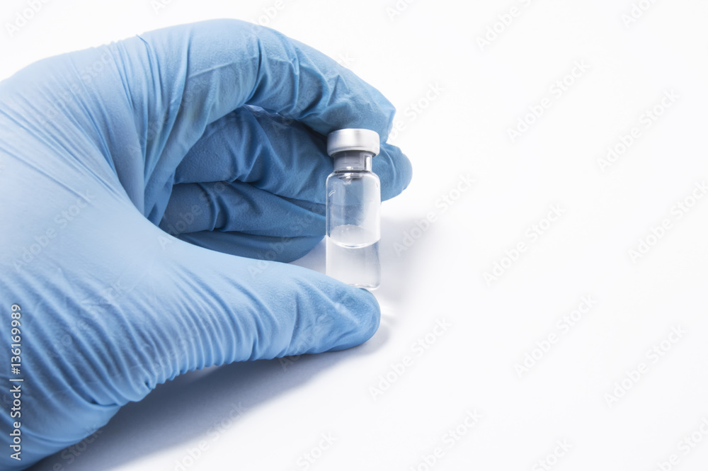 Transparent vial or bottle with the vaccine is in the doctor's hand, which is dressed in blue medical gloves. The concept of vaccination, research or production of vaccines against various diseases Transparent vial or bottle with the vaccine is in the doctor's hand, which is dressed in blue medical gloves. The concept of vaccination, research or production of vaccines against various diseases