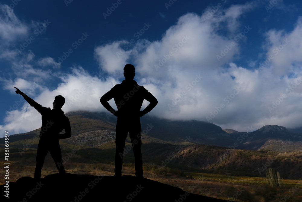 silhouette of two men standing on a rock looking into the distance
