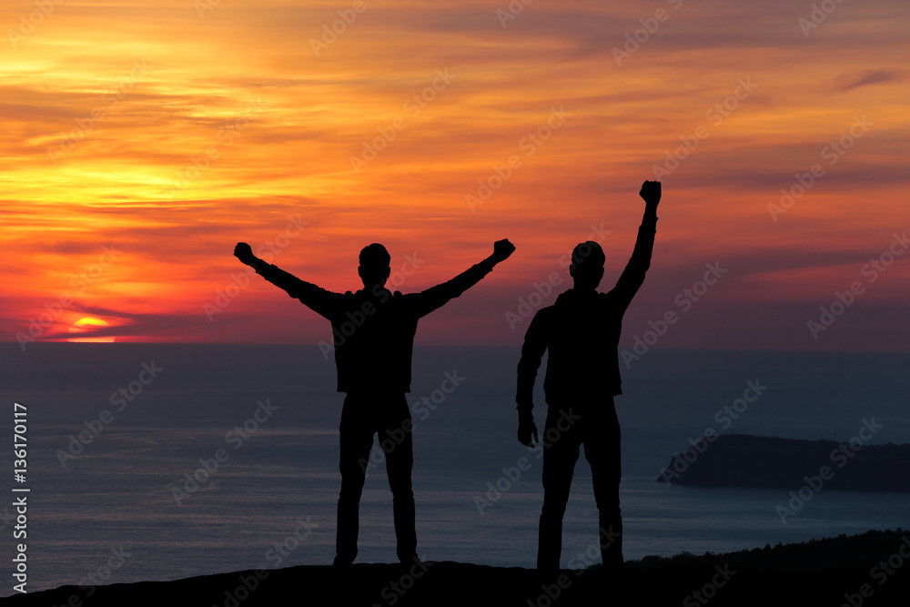 Fototapeta premium silhouette of two men standing on a rock looking into the distance