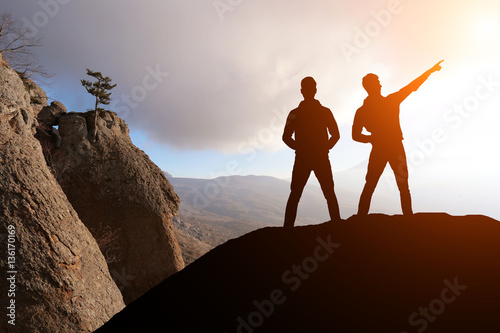 silhouette of two men standing on a rock looking into the distance