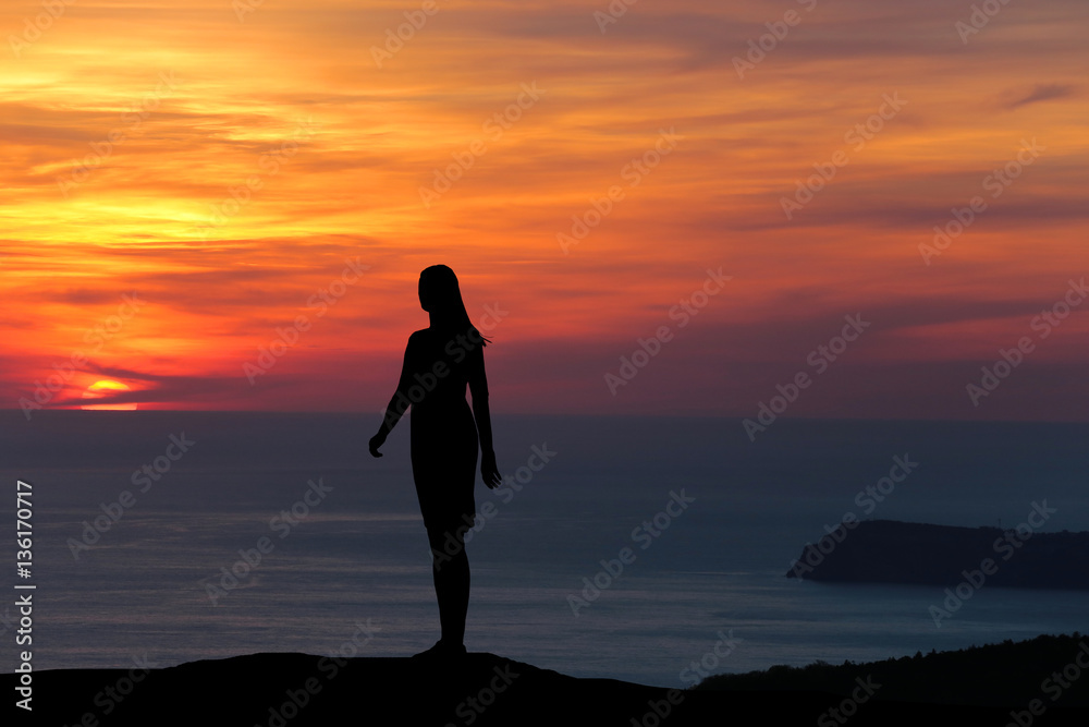 silhouette of a girl standing on a hill looking directly at the background of a beautiful sunset and the sea