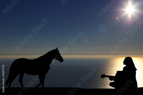 silhouette of a horse walks by the sea and a girl playing a guitar on a background of a beautiful sunset