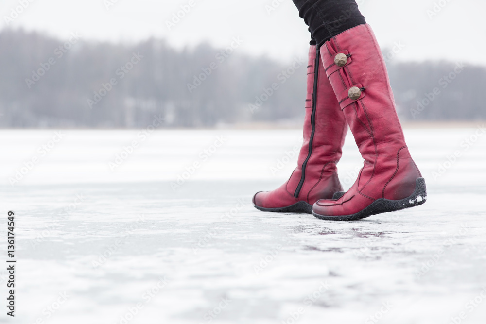 Woman walking on the lake ice surface in winter day. Red winter boots on legs. Active lifestyle at nature. Woman walking on the lake ice surface in winter day. Red winter boots on legs. Active lifestyle at nature.