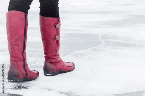 Woman walking on the lake ice surface in winter day.  Red winter boots on legs. Active lifestyle at nature.