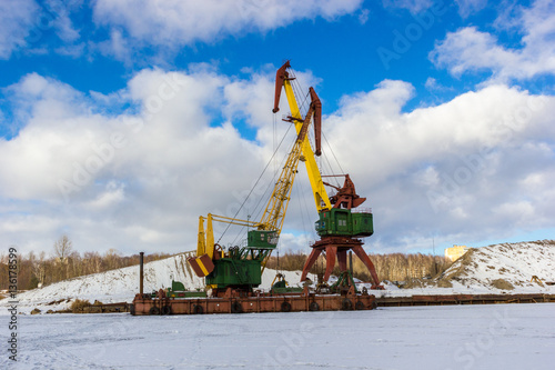 Two cranes Dockside crane and floating crane standing idle in winter. Frozen River does not allow them to work.