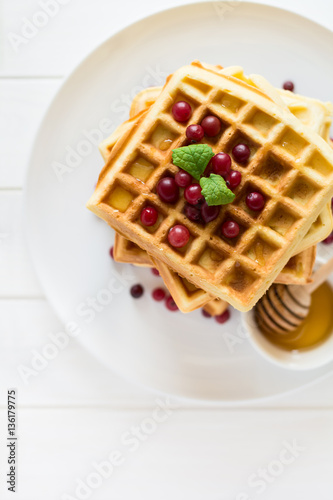 Belgian waffles with honey and cranberries on white plate. Selective focus