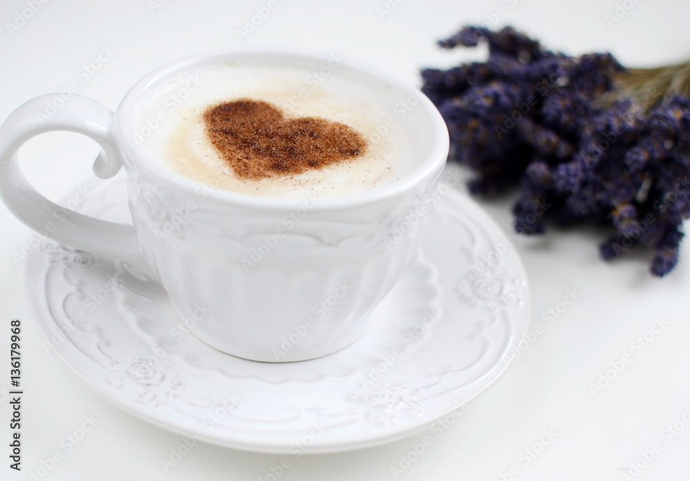 Cappuccino with heart pattern of cinnamon and flowers composition on the white table Cappuccino with heart pattern of cinnamon and flowers composition on the white table