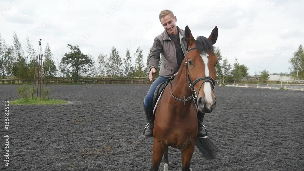 Male jockey riding sitting top and caresses and petting the neck of animal. Young man stroking mane of horse outdoor. Care and love for the animals. Close up Slow motion Male jockey riding sitting top and caresses and petting the neck of animal. Young man stroking mane of horse outdoor. Care and love for the animals. Close up Slow motion