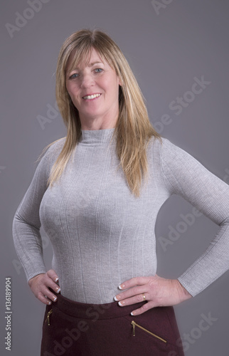 Attractive middle aged busty woman with hands on waist wearing a tight grey jumper