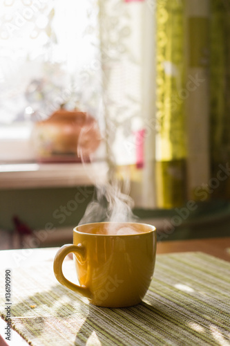 Steam of morning tea above yellow cup on table