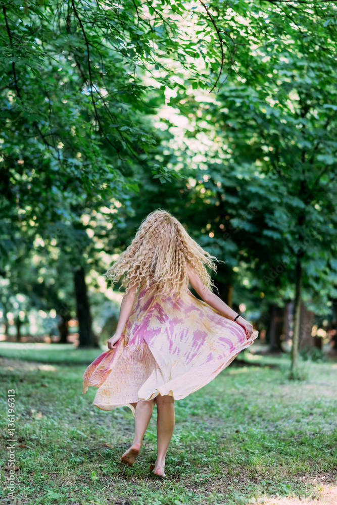 Back view of young beautiful caucasian blonde long hair woman playing in the forest wearing long pink dress - moving, freedom, serene concept Back view of young beautiful caucasian blonde long hair woman playing in the forest wearing long pink dress - moving, freedom, serene concept