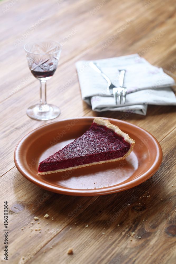 Piece of rustic berry tart on brown plate, on wooden table.